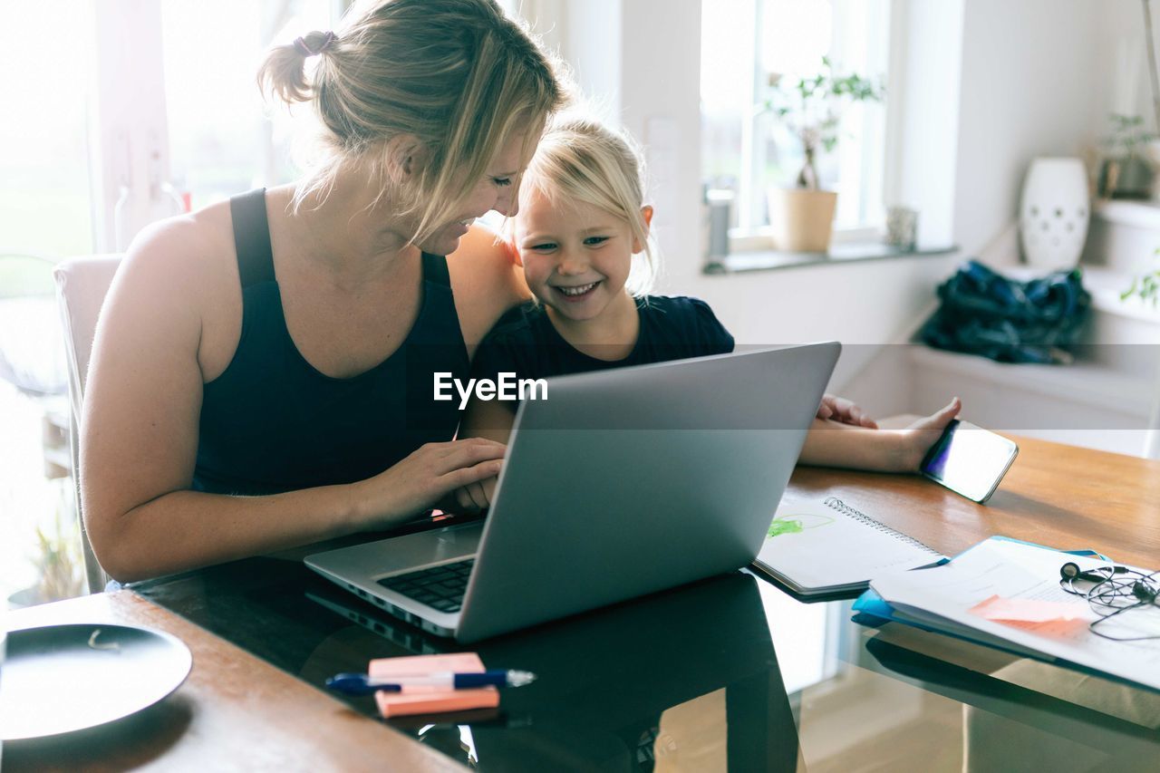 Daughter looking at laptop while sitting by mother at home