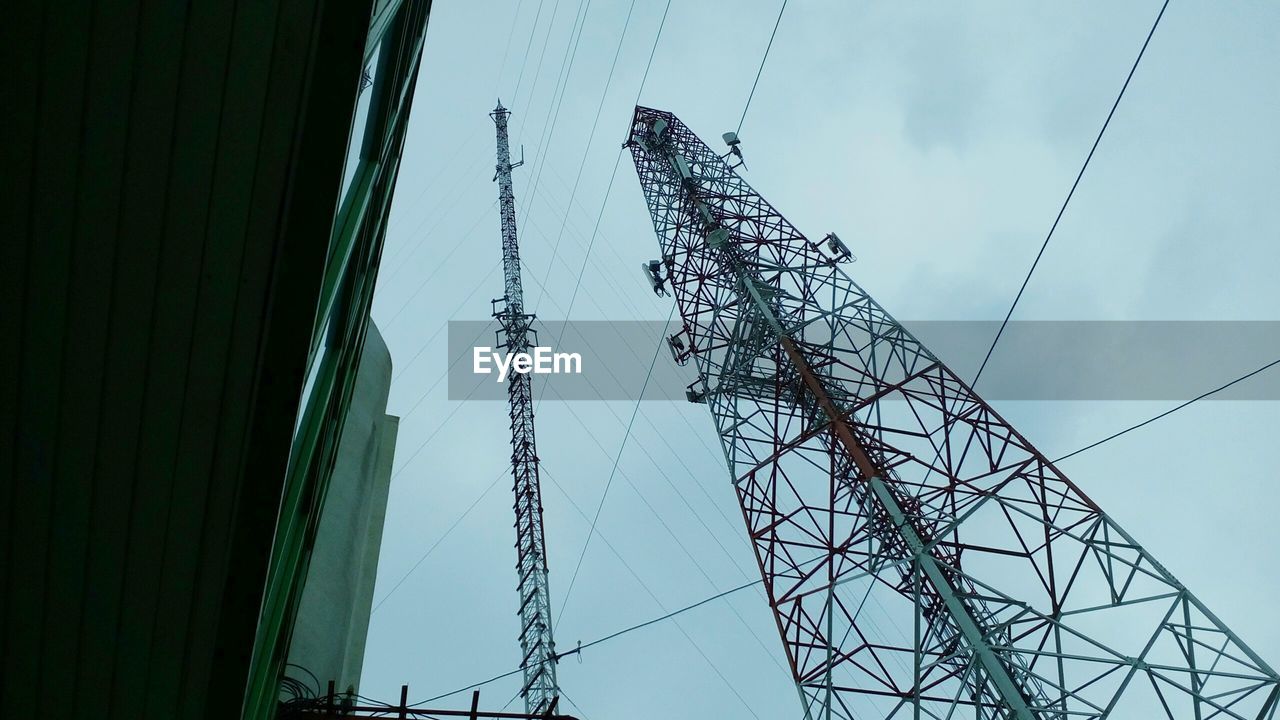 Low angle view of communications towers and building against cloudy sky