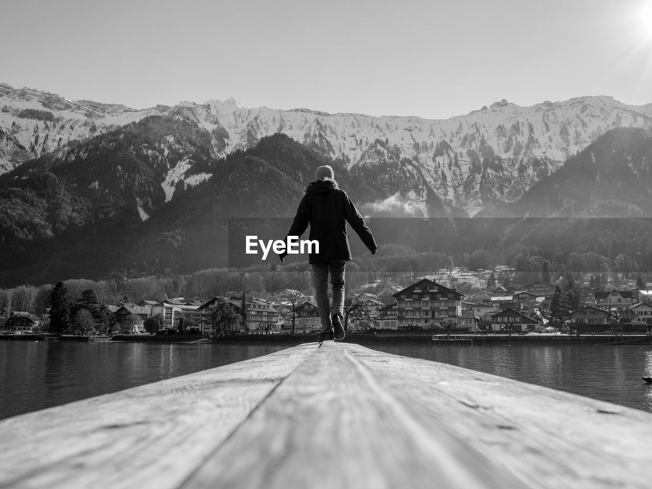 Rear view of person walking on pier over lake against mountains