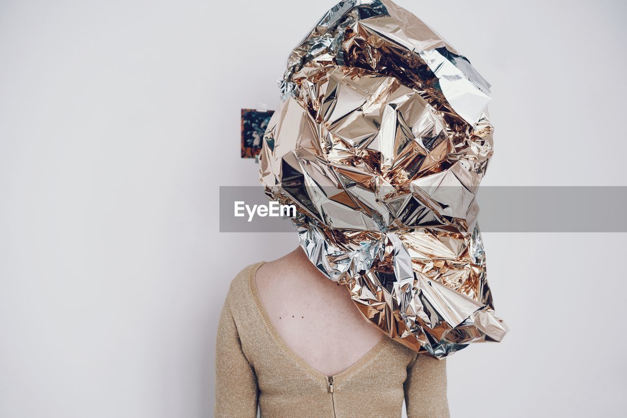 Rear view of woman covered in wrapping paper against white wall