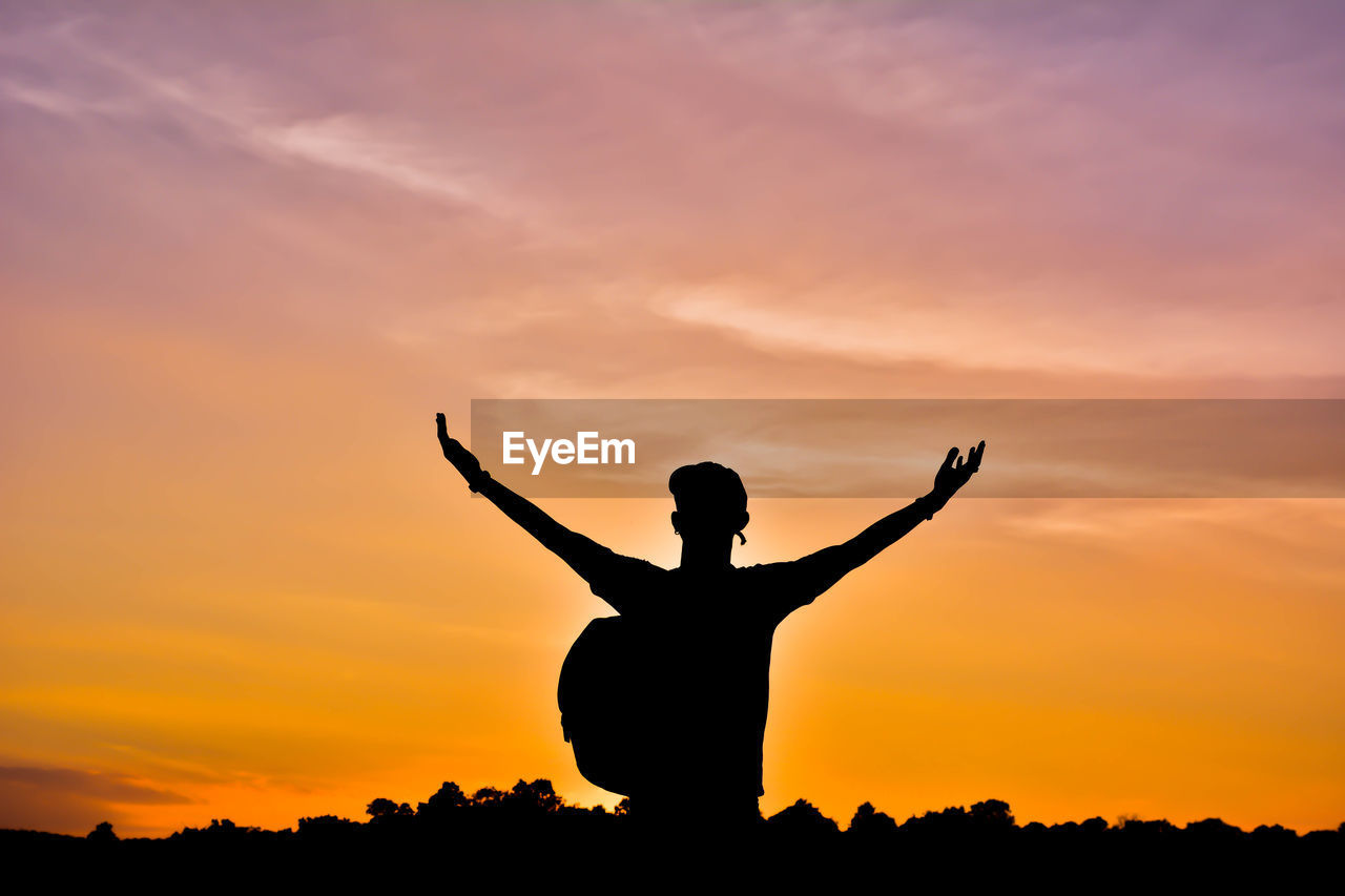 Silhouette man with arms outstretched against cloudy sky during sunset