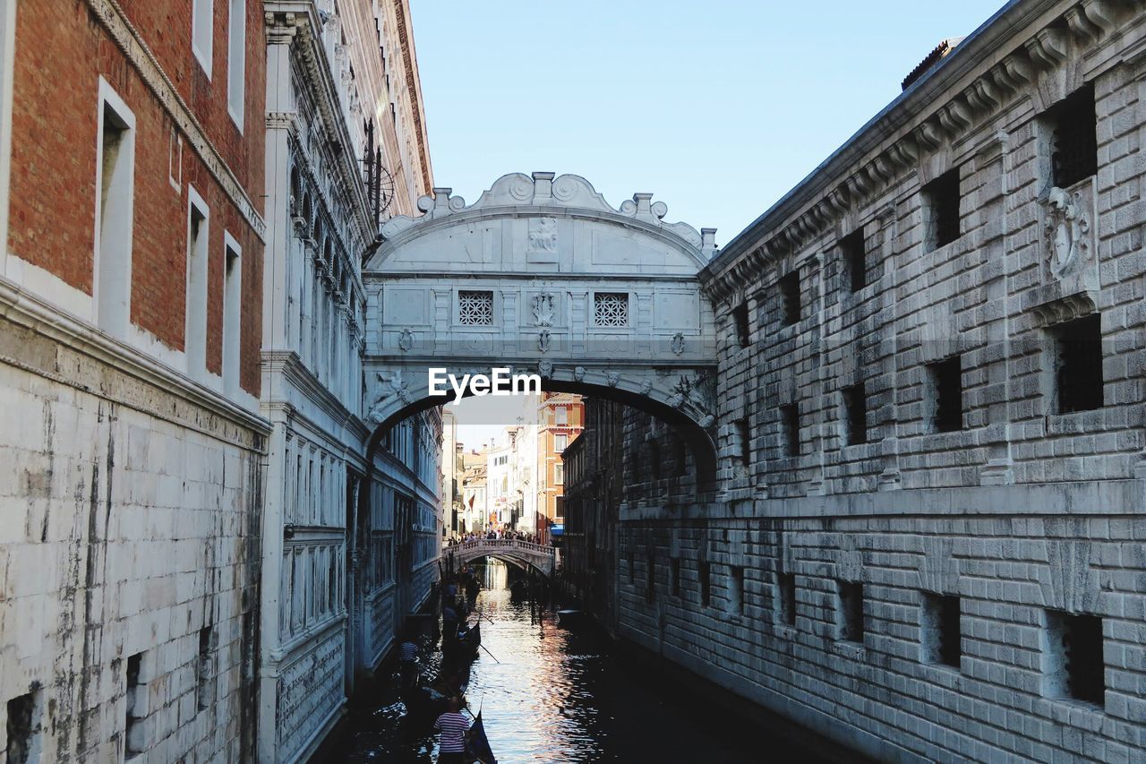 Arch bridge over canal amidst buildings against sky