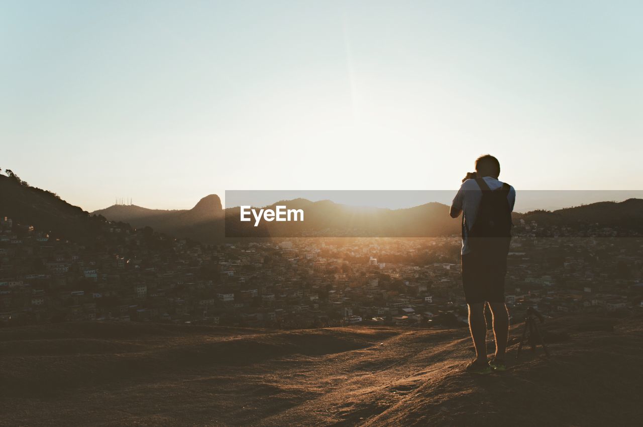 Rear view of man photographing on mountain against clear sky during sunset