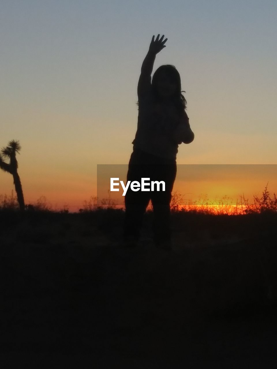 SILHOUETTE WOMAN STANDING ON FIELD AGAINST ORANGE SKY