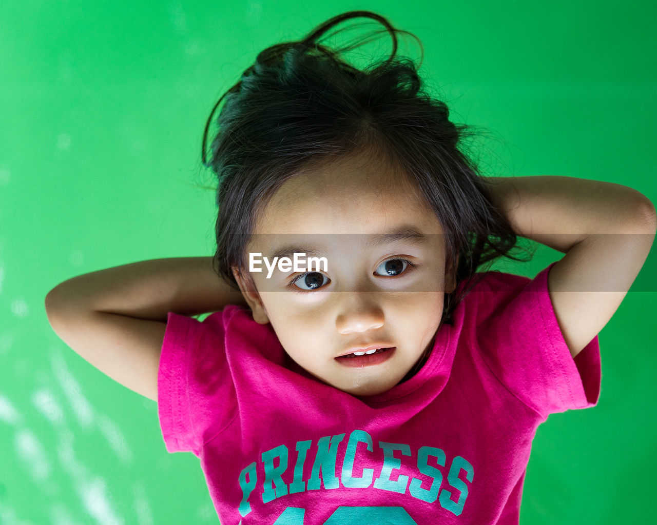 High angle view of cute girl with hands behind head lying on green background