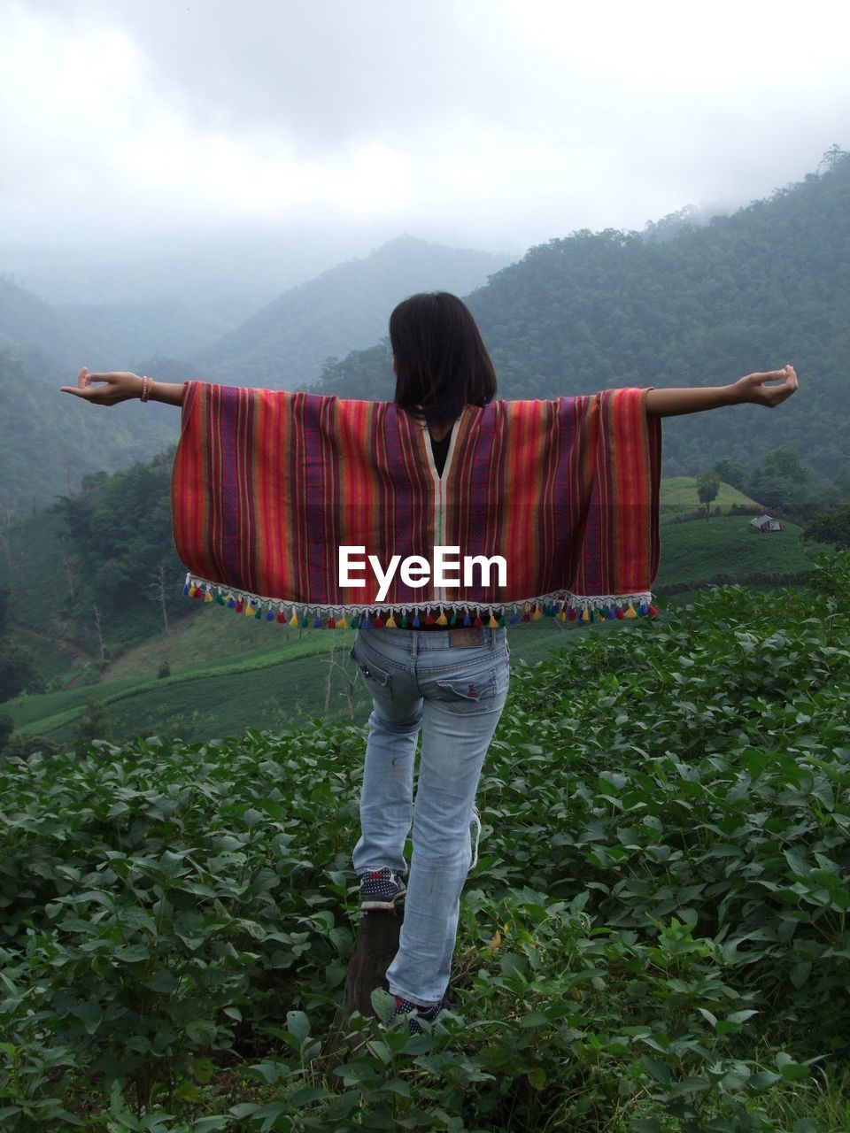 Rear view of woman with arms outstretched walking on field