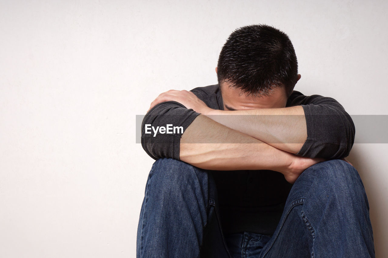 Depressed man sitting against wall