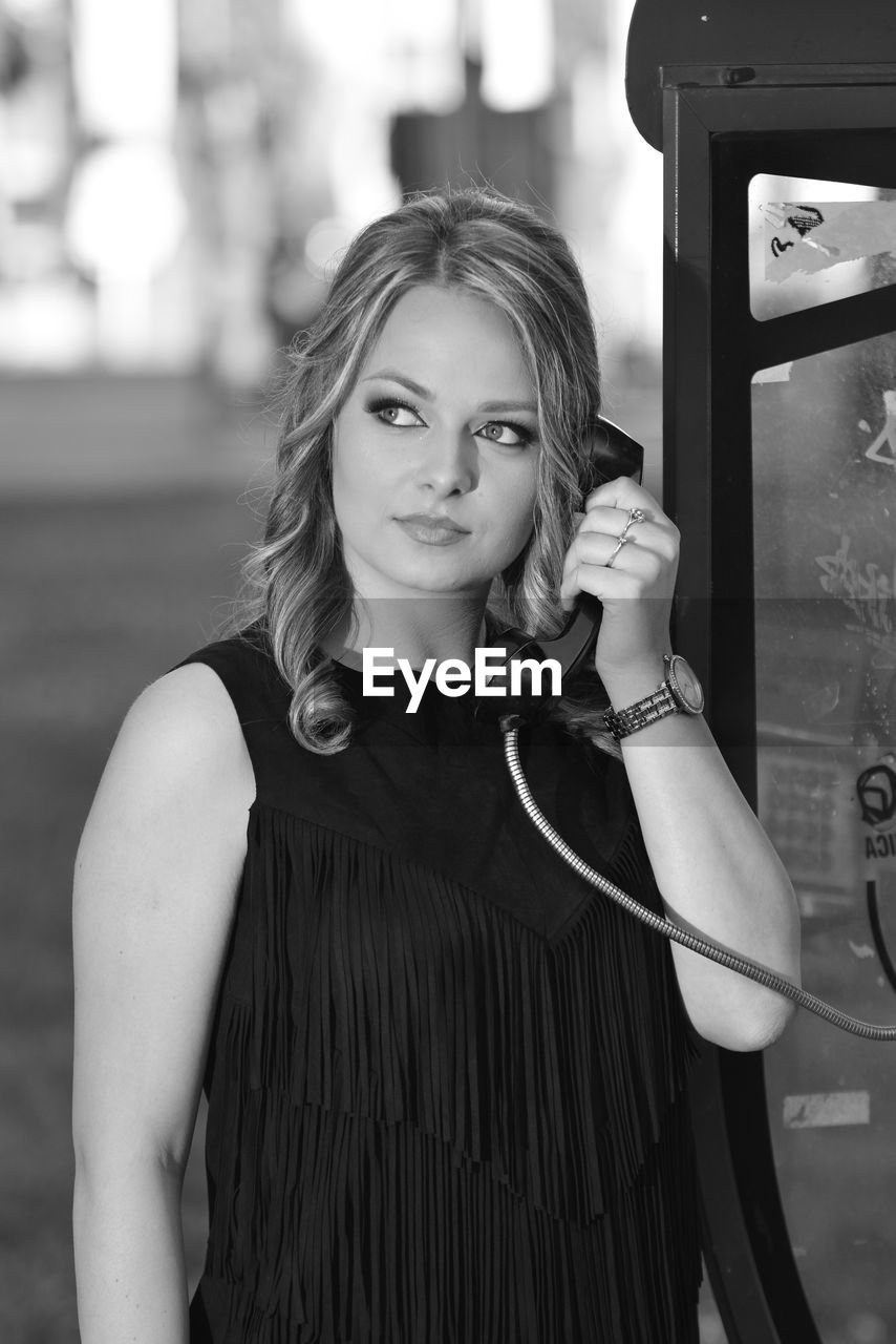 Portrait of young woman standing outdoors by the telephone booth