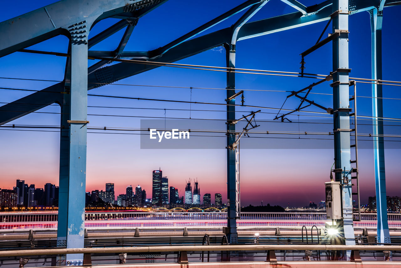 Illuminated bridge and buildings against sky at dusk