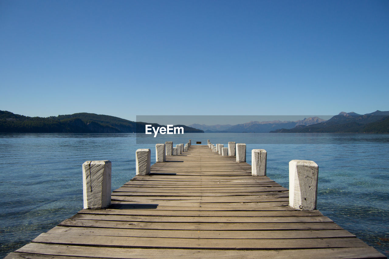 Pier over lake against clear blue sky