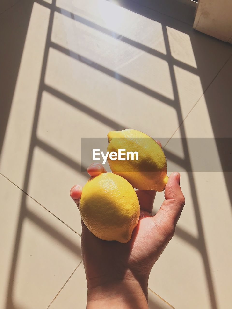 Cropped hand holding lemons against wall