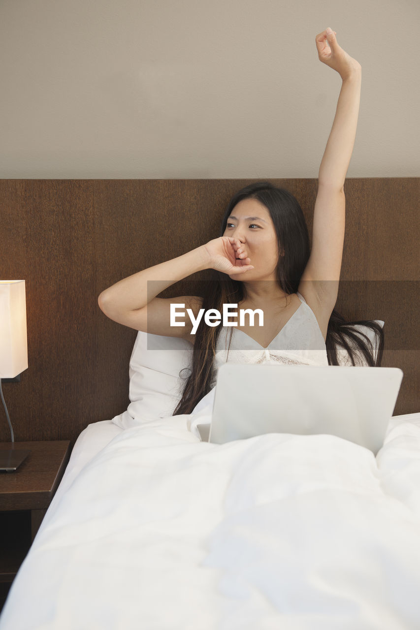 Beautiful woman waking up and checking her laptop in hotel room