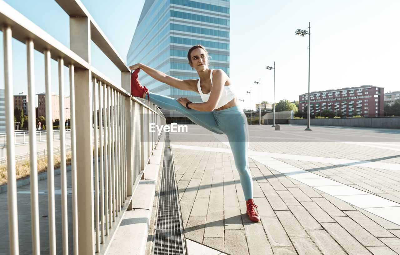 Young woman stretching on railing in city