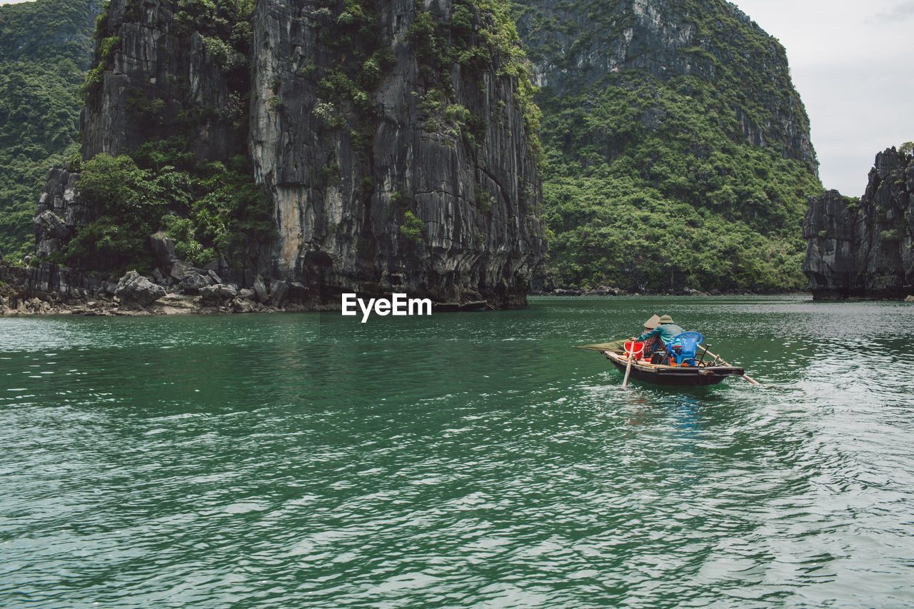 People rowing boat on halong bay against rocky mountains