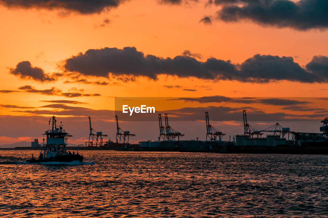 CRANES AT HARBOR AGAINST ORANGE SKY