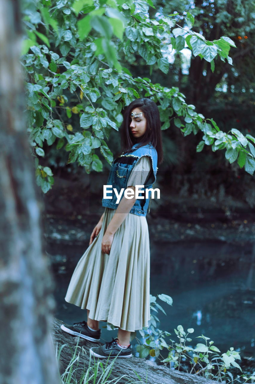 Side view of girl standing by plant in forest