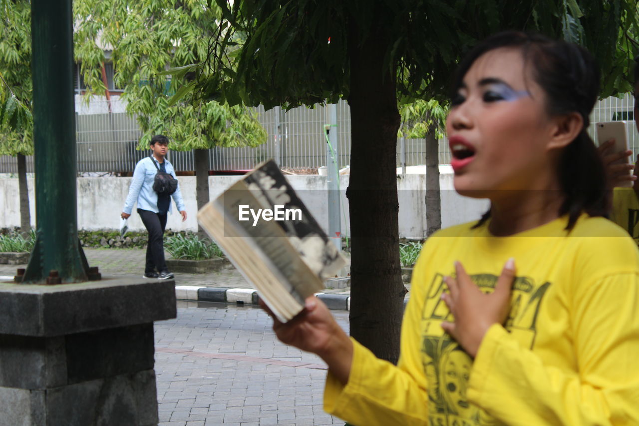 Woman reading book against trees