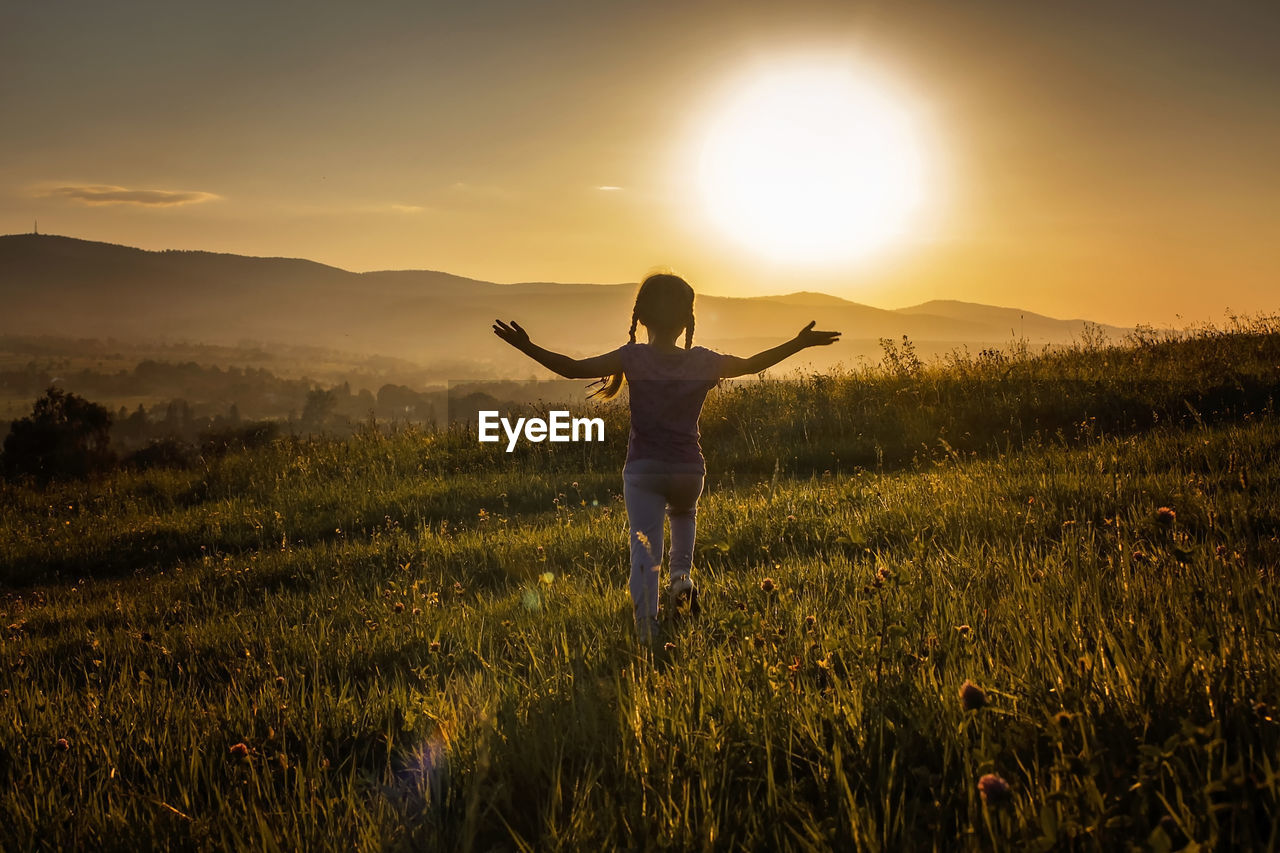 Rear view of woman standing on field against sky during sunset