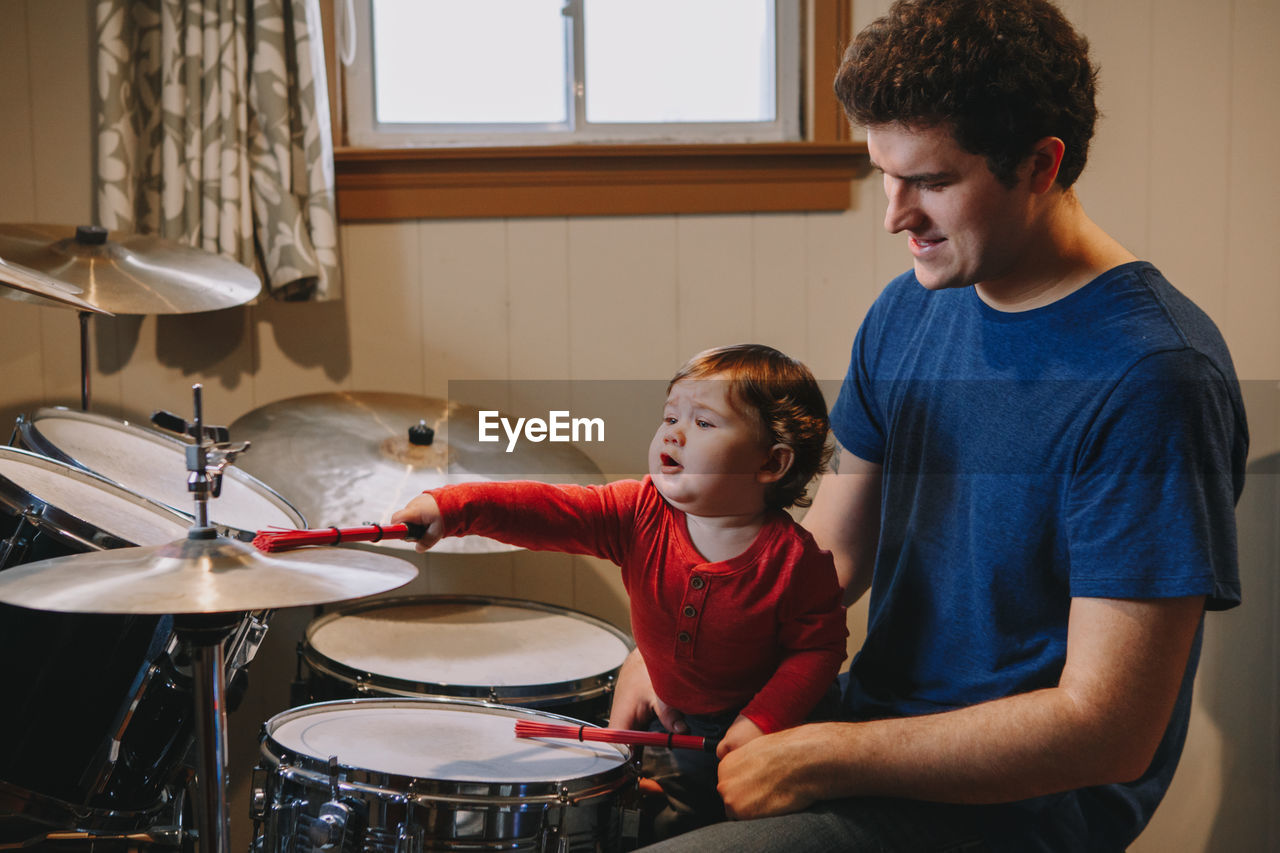 Cute boy playing drum while sitting with father at home