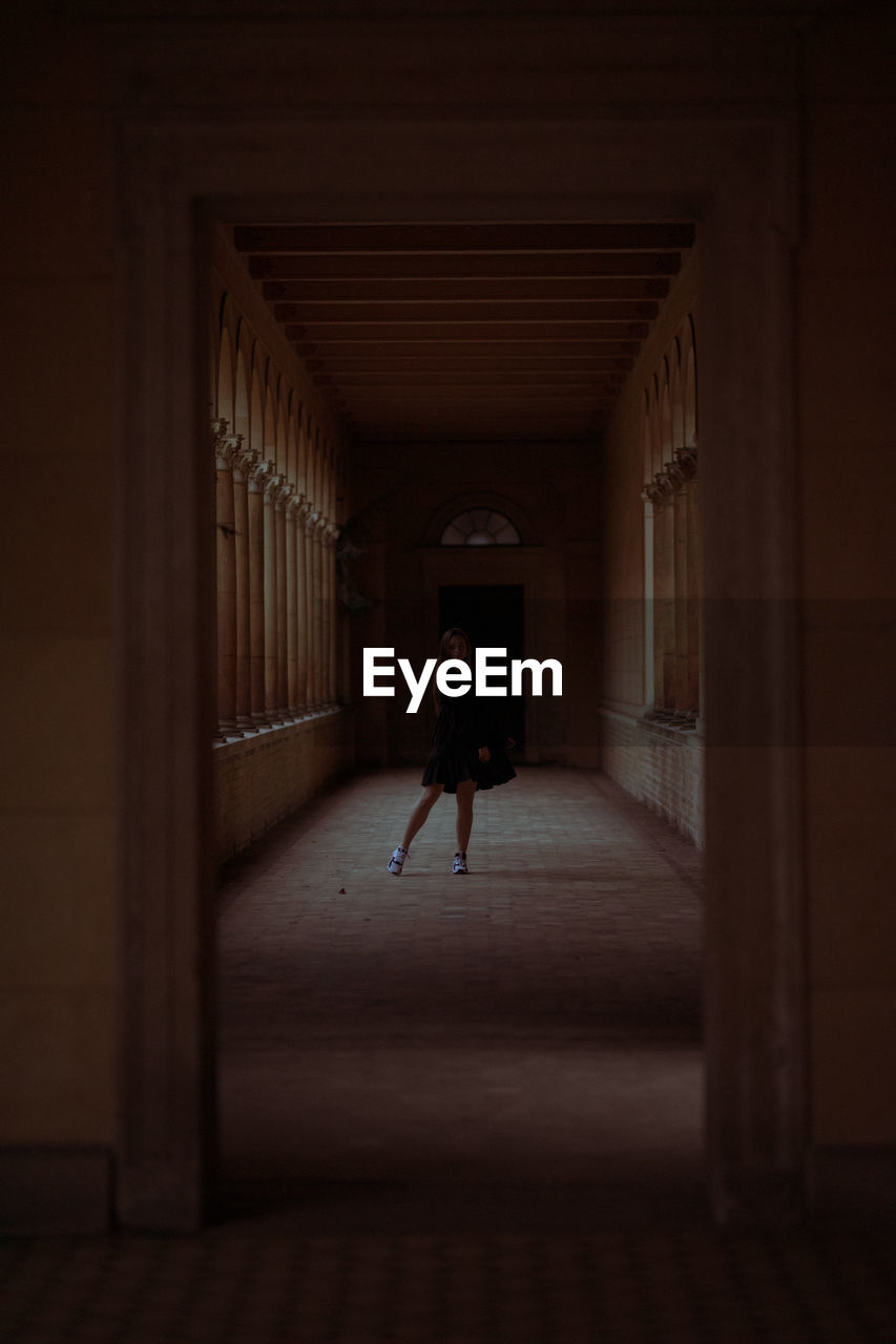 Full length of young woman standing in dark corridor