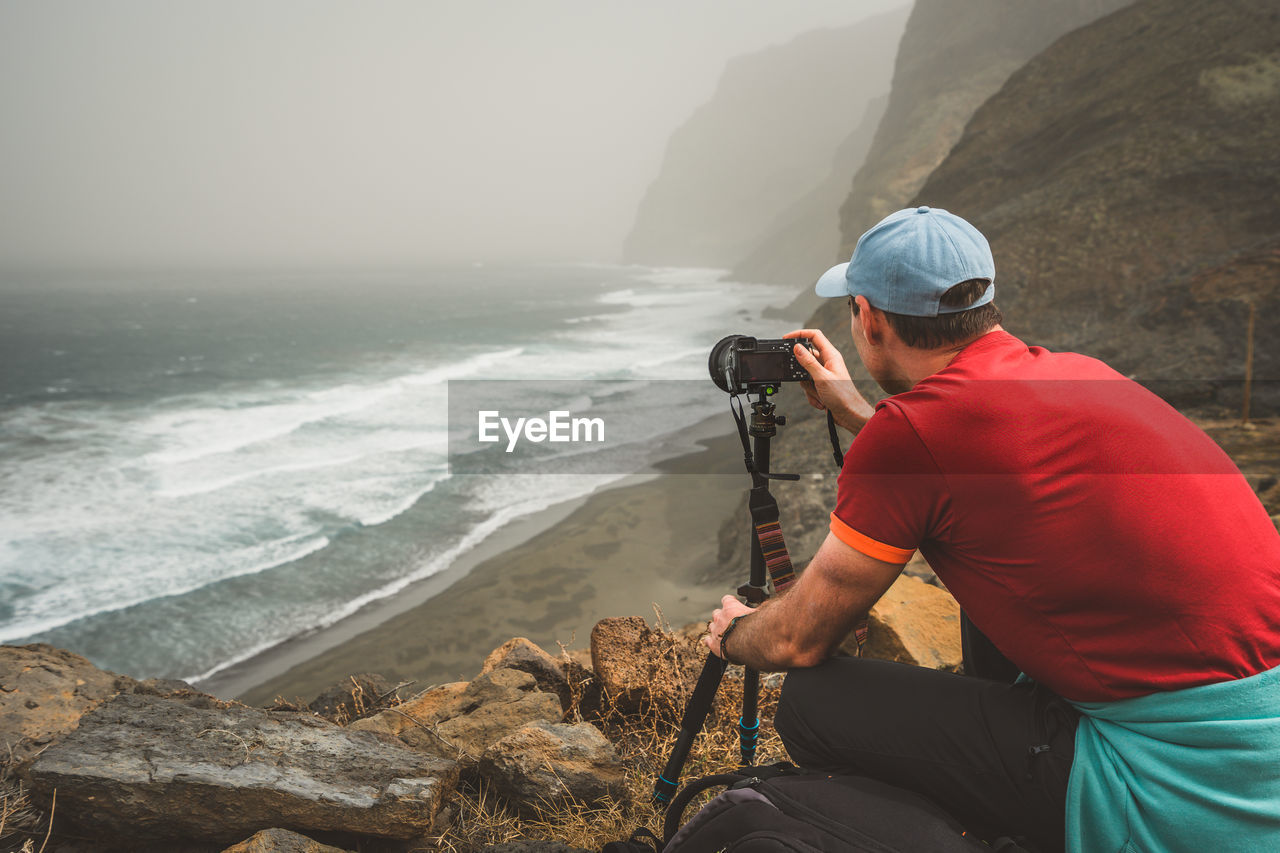 Man photographing sea with camera on rock at beach