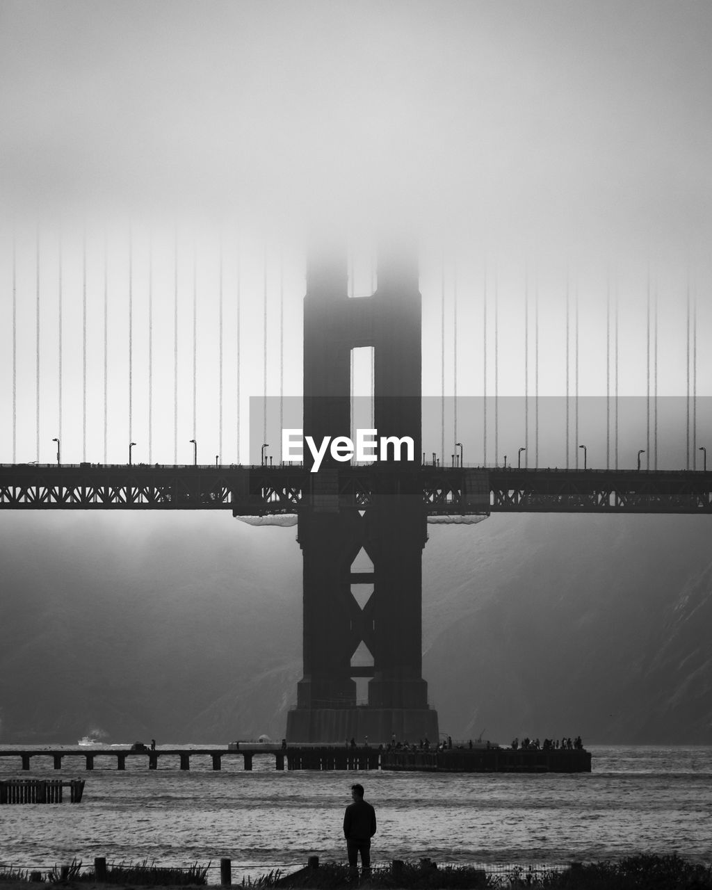 Silhouette man standing by river against bridge