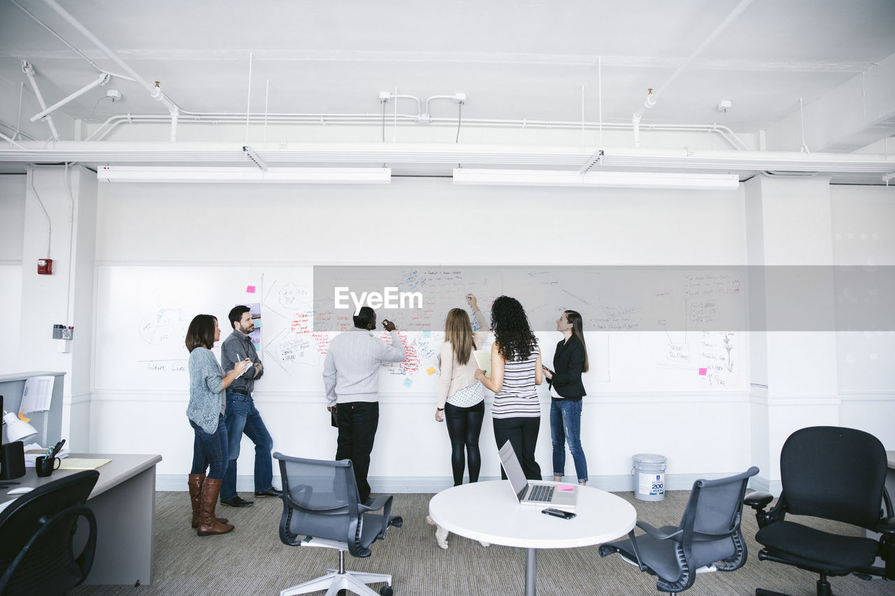 Business people writing notes on whiteboard while brainstorming in meeting at office