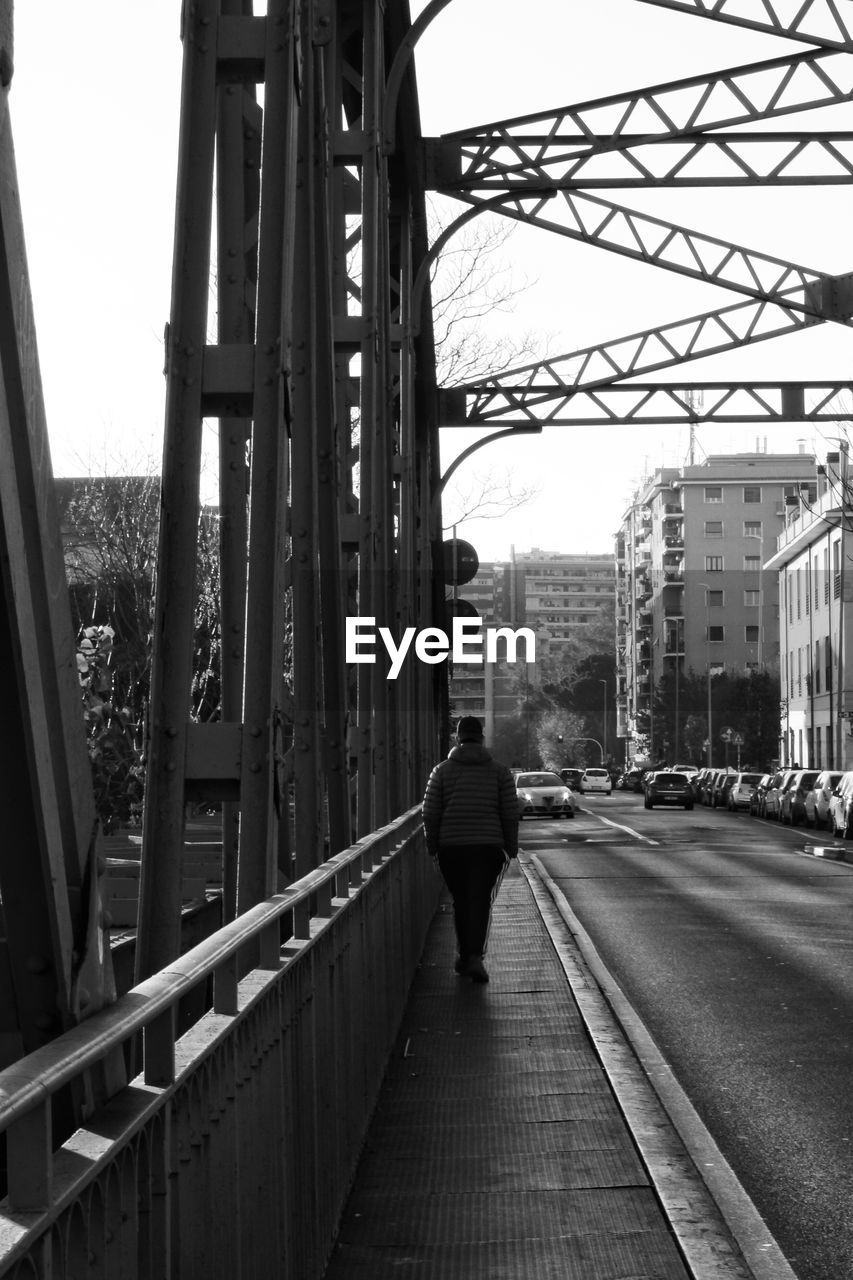 FULL LENGTH REAR VIEW OF MAN WALKING ON BRIDGE IN CITY