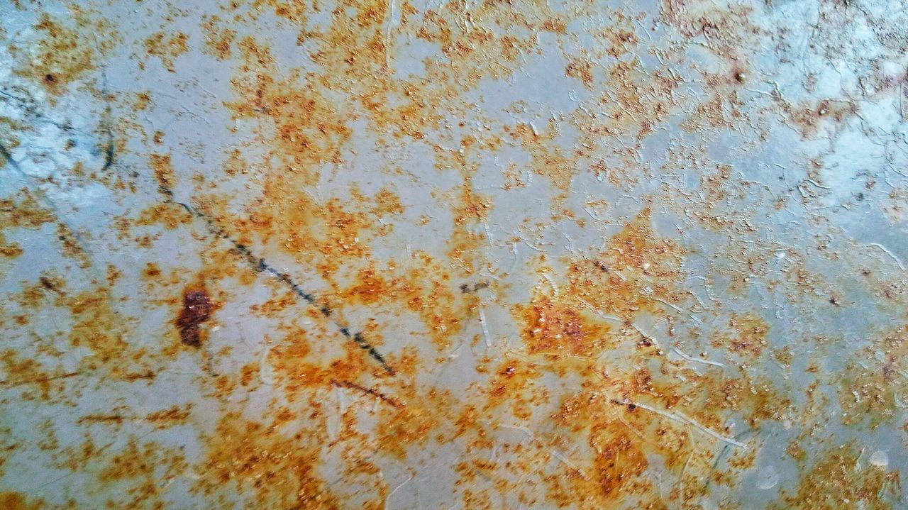FULL FRAME SHOT OF RUSTY METAL ON WEATHERED WALL