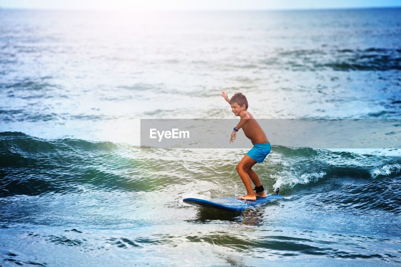 side view of shirtless boy surfing in sea