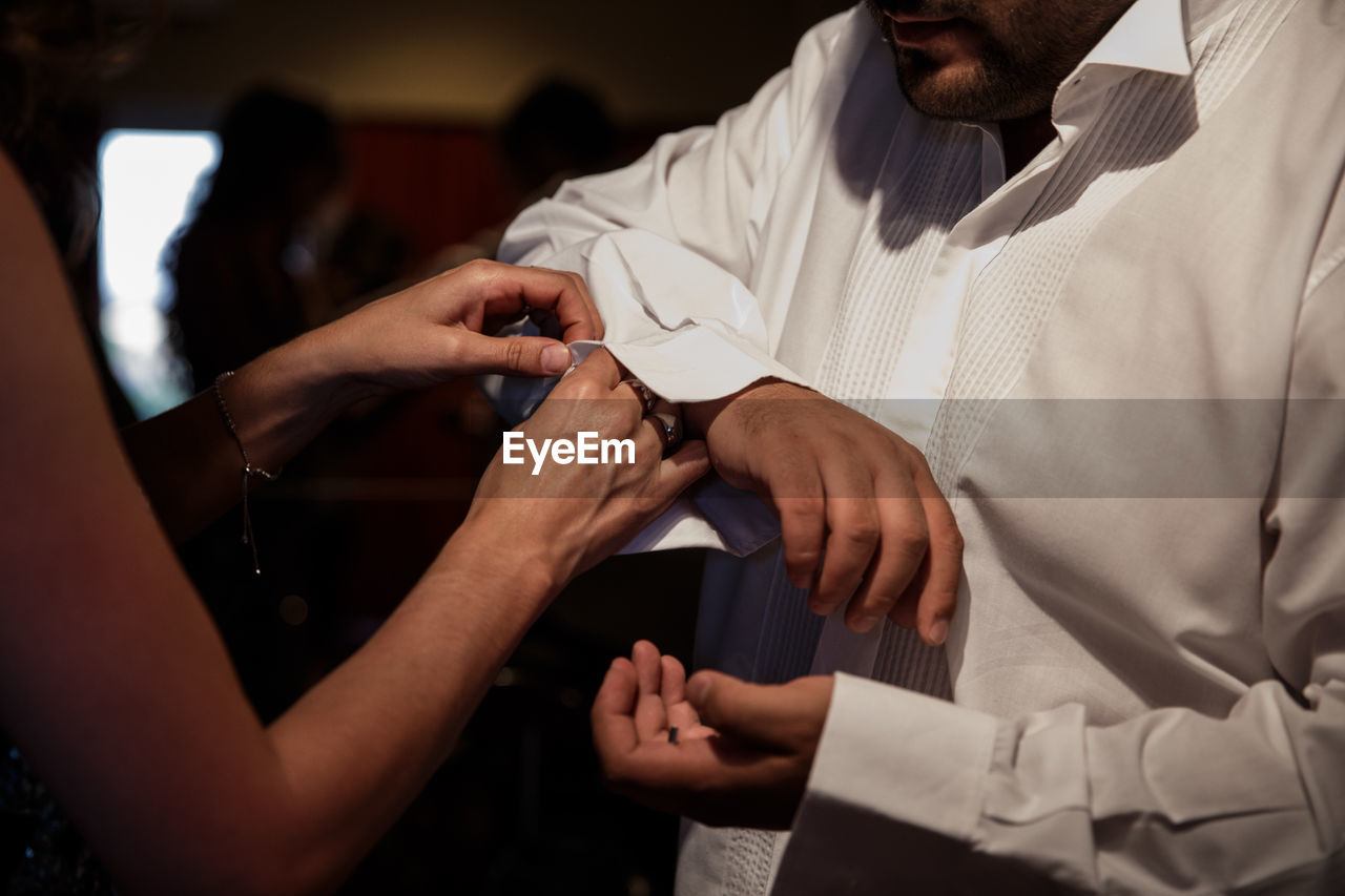 Cropped image of woman buttoning bridegroom shirt at home