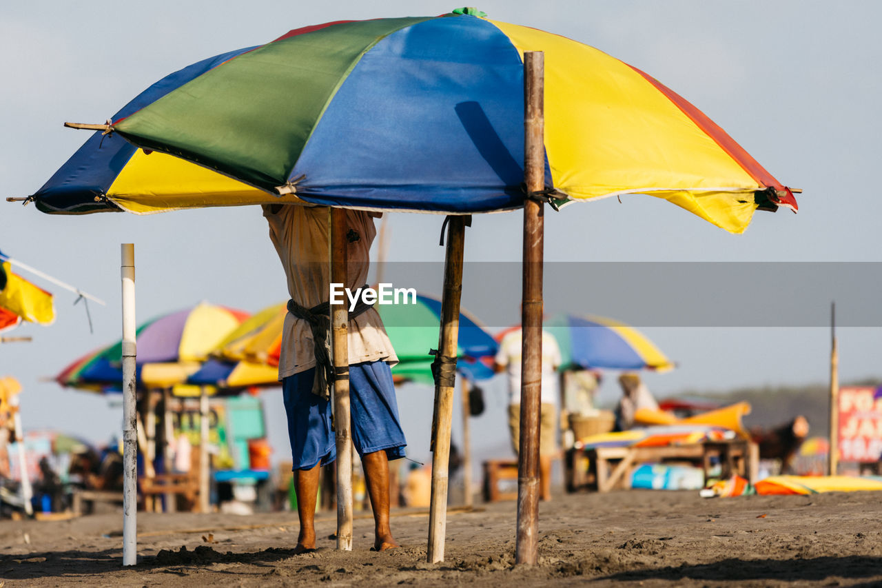 umbrella, protection, parasol, land, beach, security, sunshade, beach umbrella, water, nature, sand, shade, summer, sky, trip, vacation, rain, wet, fashion accessory, holiday, day, sea, adult, relaxation, chair, outdoors, travel destinations, leisure activity, yellow, multi colored, focus on foreground, group of people, men, environment, travel