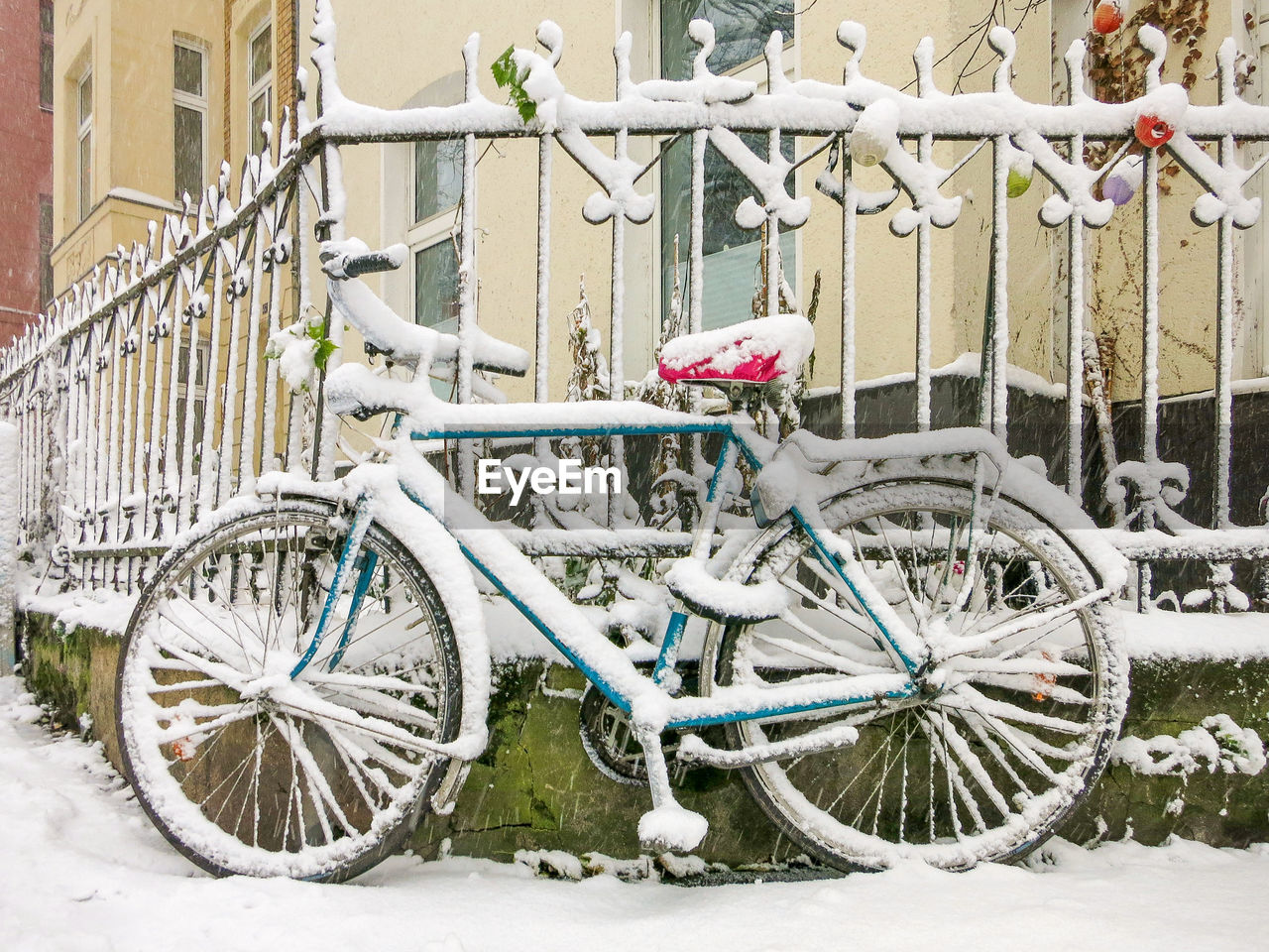 Bicycle parked on snow covered fence during winter