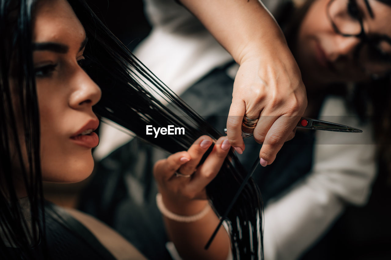 Close-up of hairdresser cutting woman hair in salon