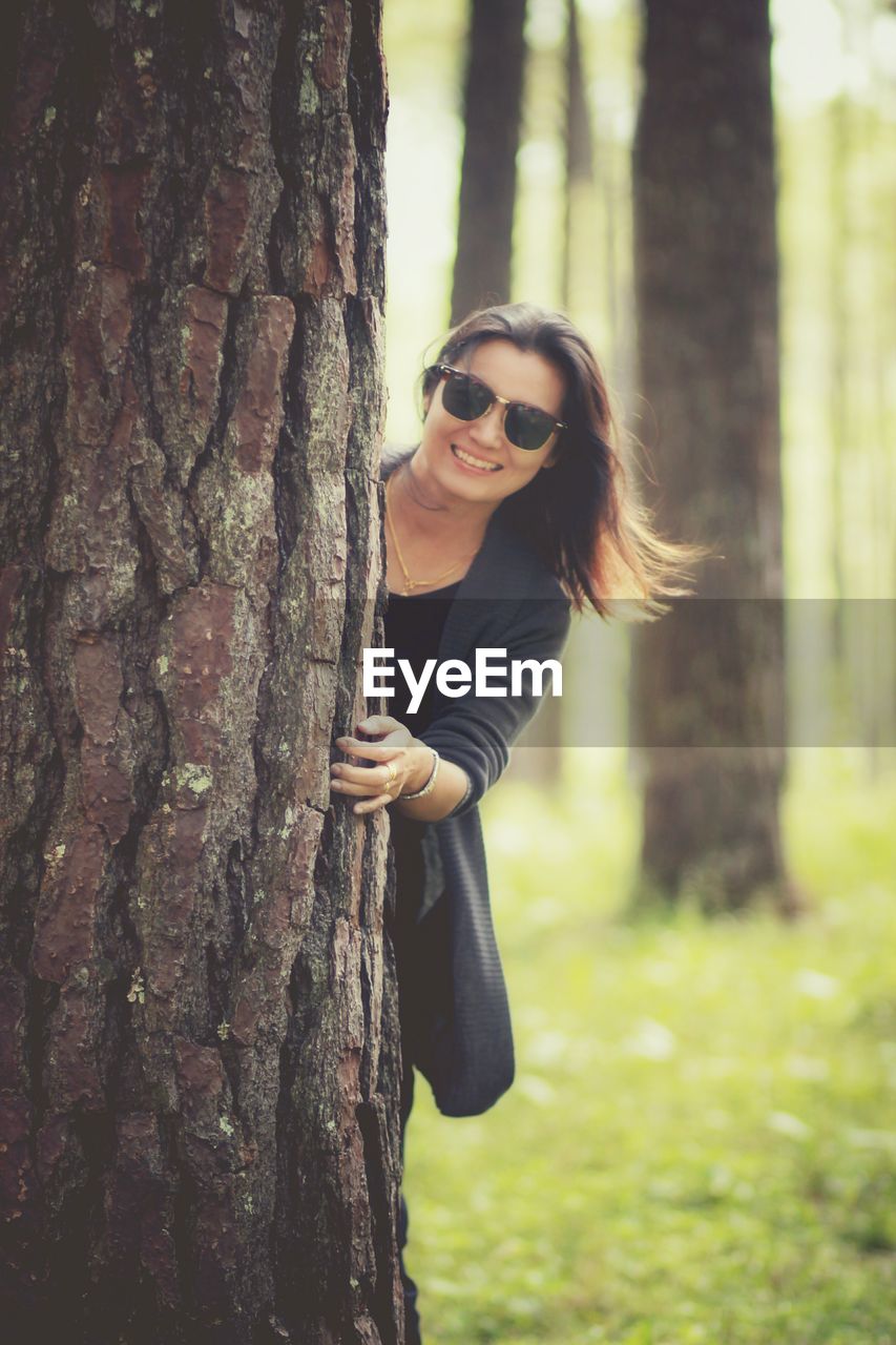 Portrait of smiling young woman holding tree trunk