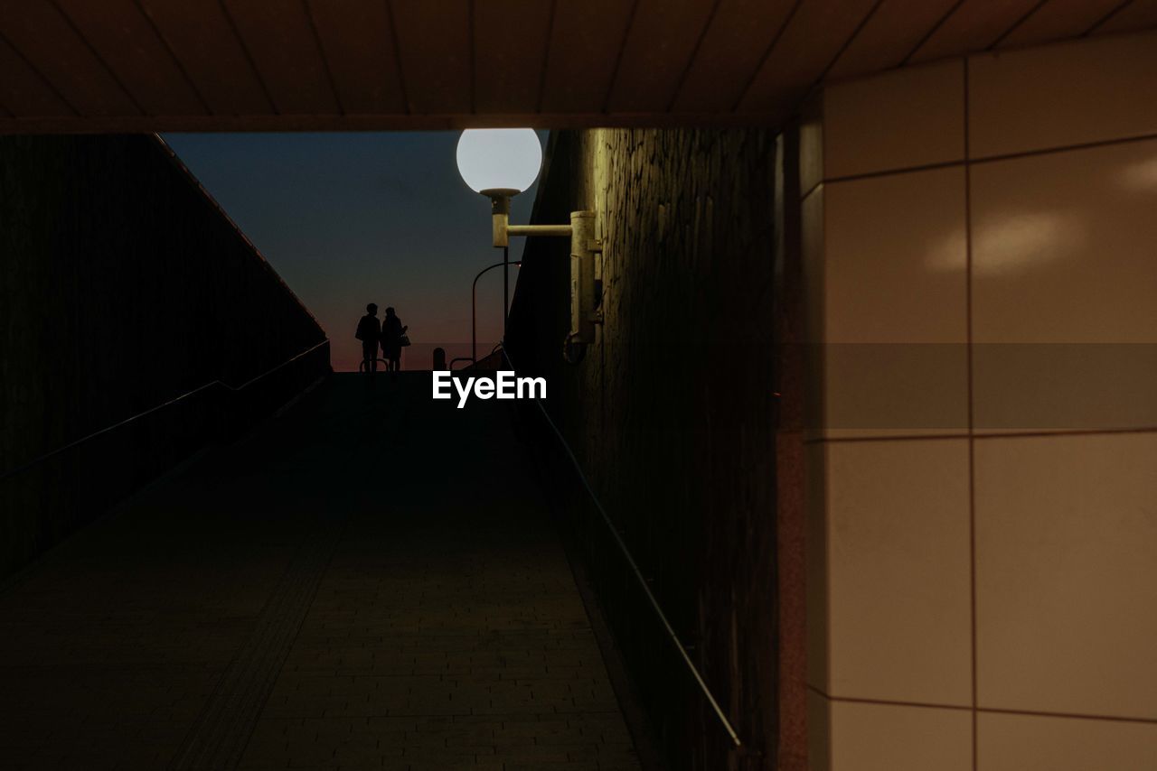 REAR VIEW OF MAN STANDING IN ILLUMINATED UNDERGROUND