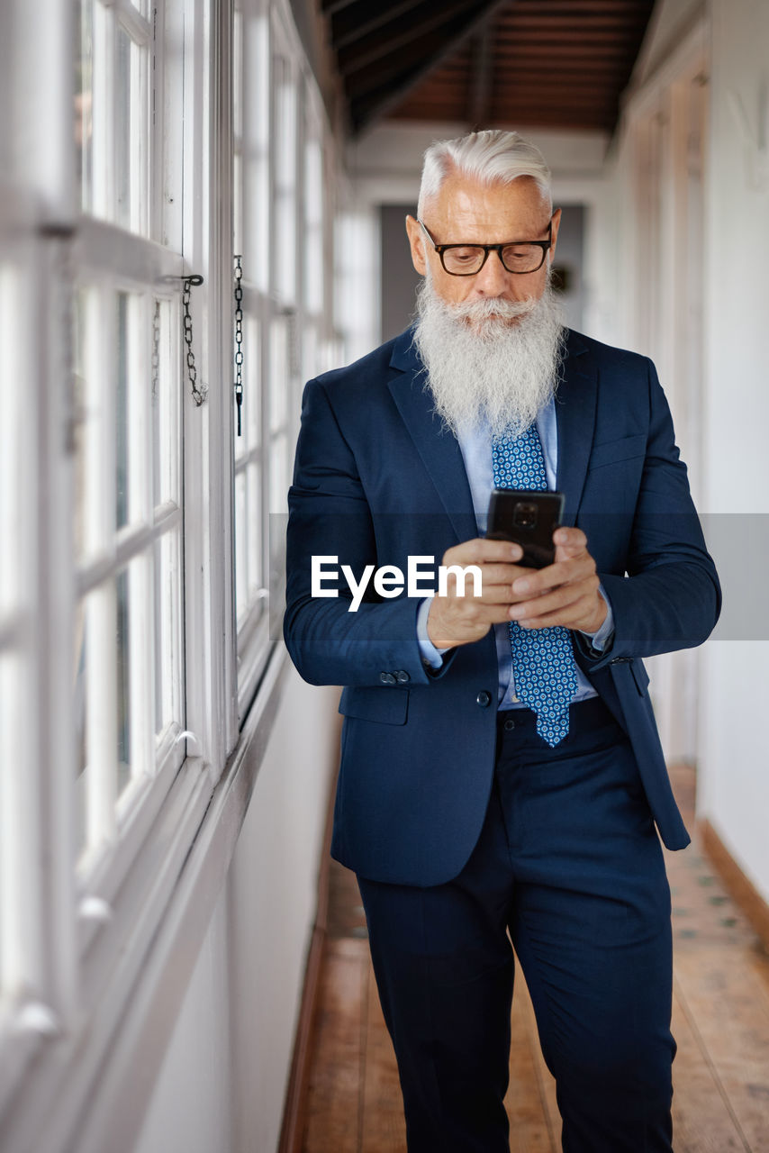 Stylish senior businessman chatting on smartphone in corridor