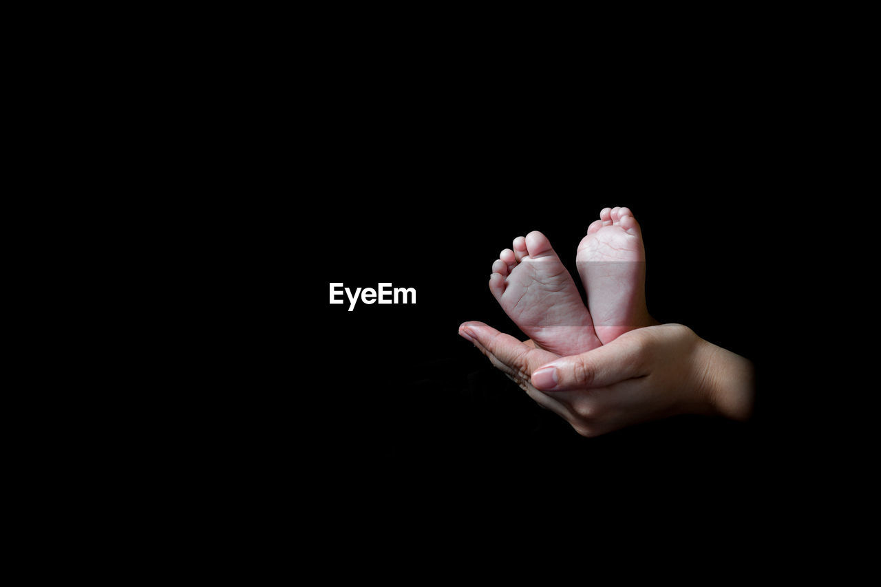 Cropped hands holding baby feet against black background