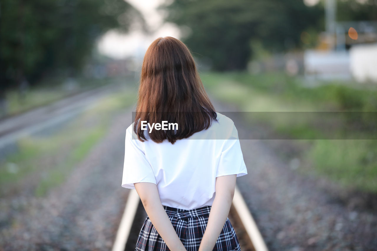 Rear view of woman standing on railroad track