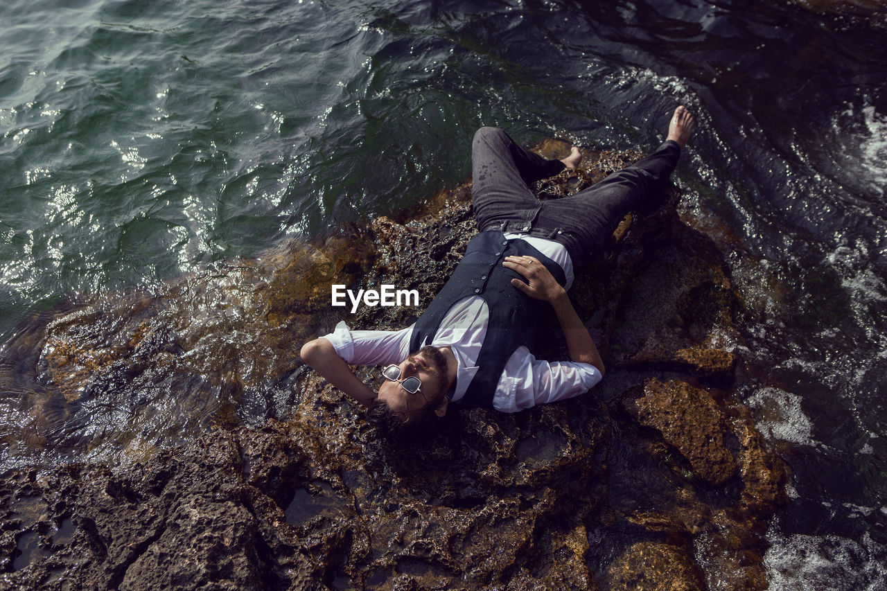 Man with a beard in dark clothes and white shirt lie on the stone seashore in the crimea tarkhankut