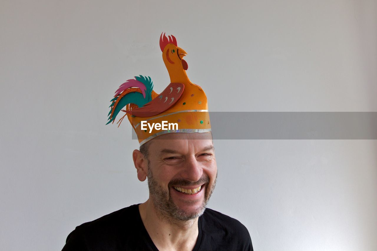 Portrait of happy man wearing rooster shape party hat against white background