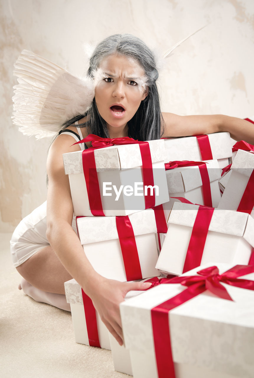 Portrait of angry female model in angel costume holding christmas presents