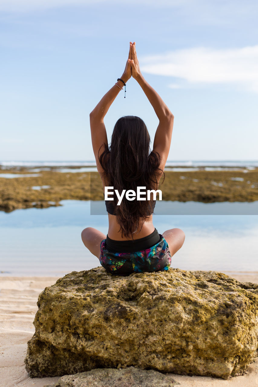 Rear view of young woman doing yoga on beach