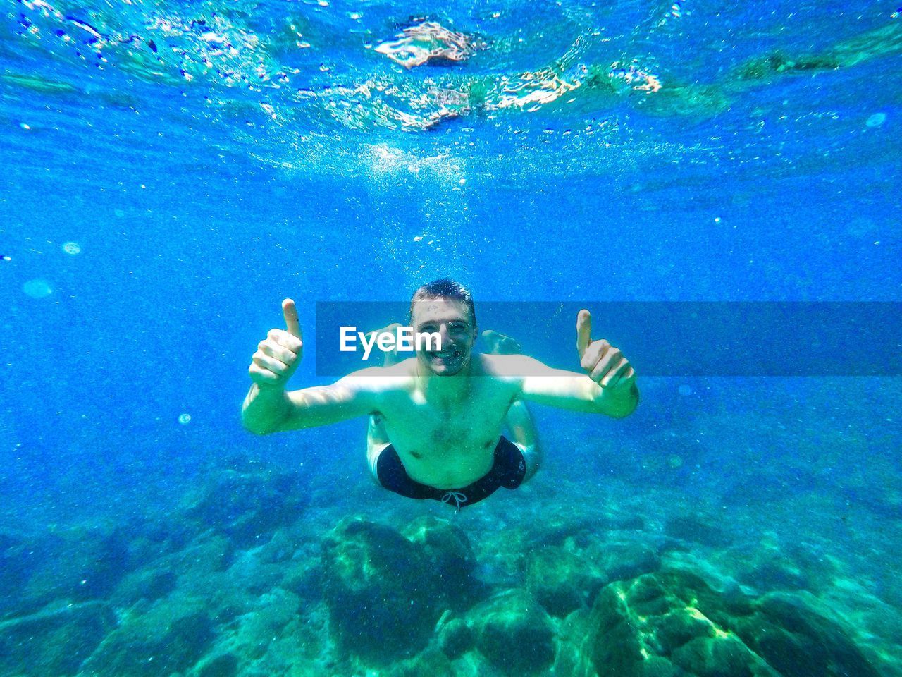 Portrait of shirtless young man gesturing thumbs up in sea