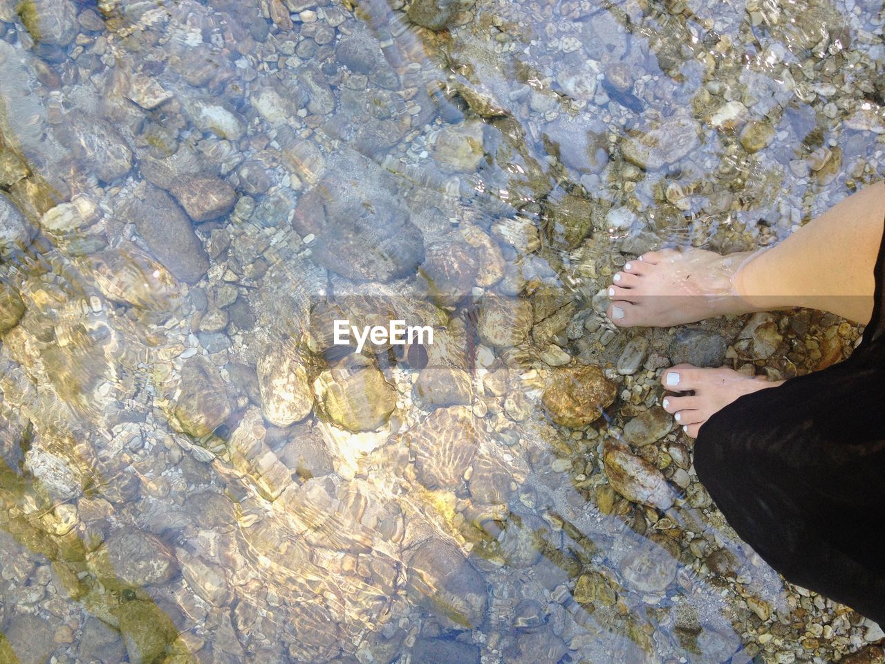 LOW SECTION OF PERSON STANDING IN WATER AT BEACH