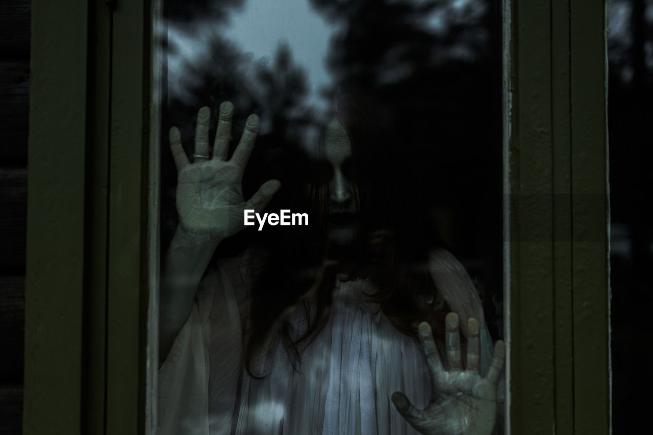 Spooky ghost looking through glass window of haunted cabin