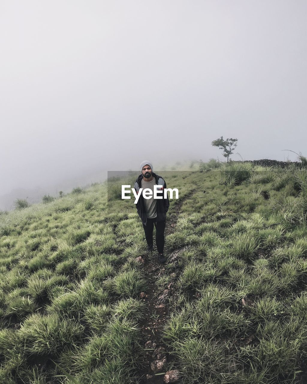 Portrait of man standing on grassy mountain against sky