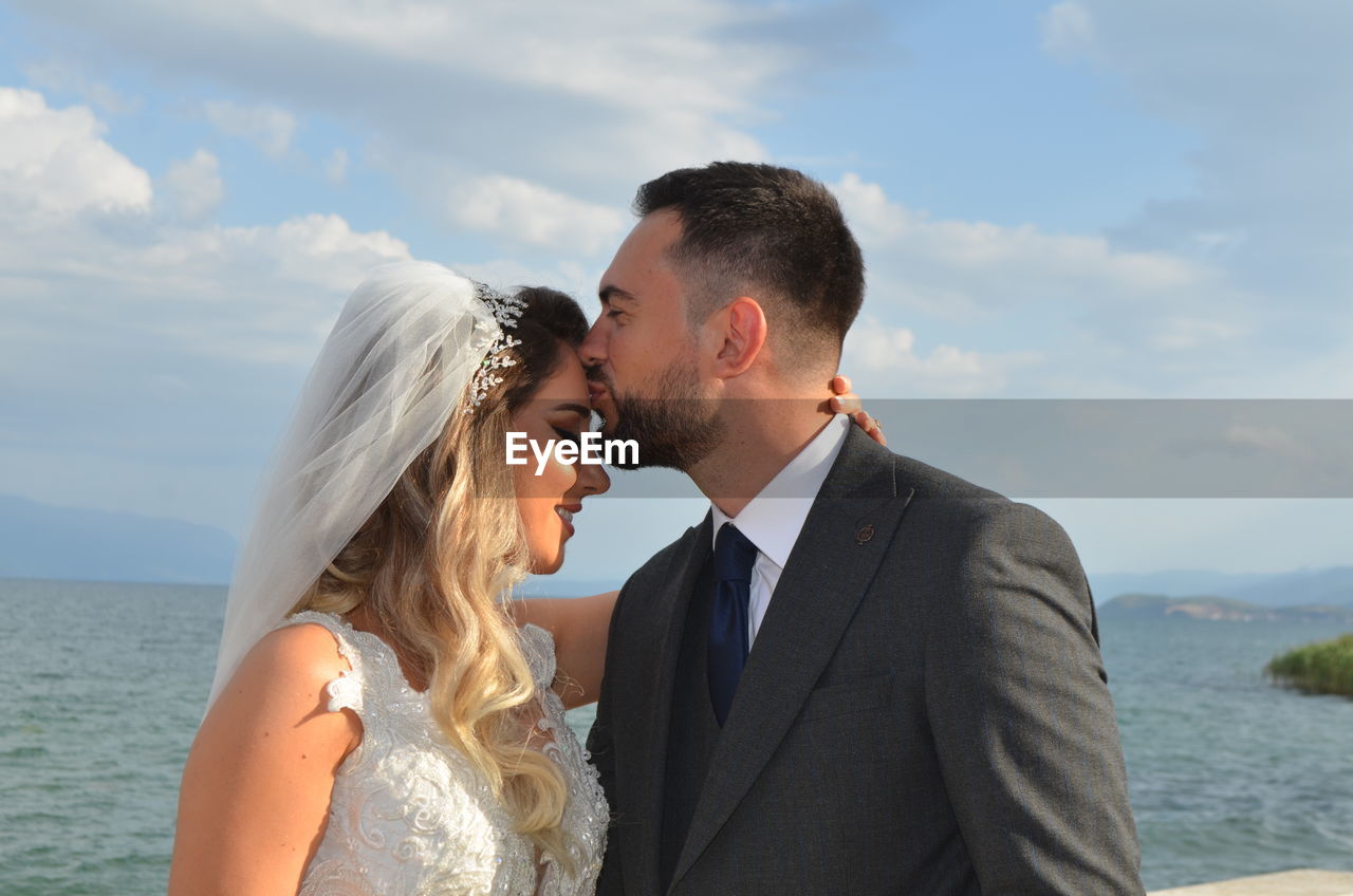 side view of couple standing at beach against sky