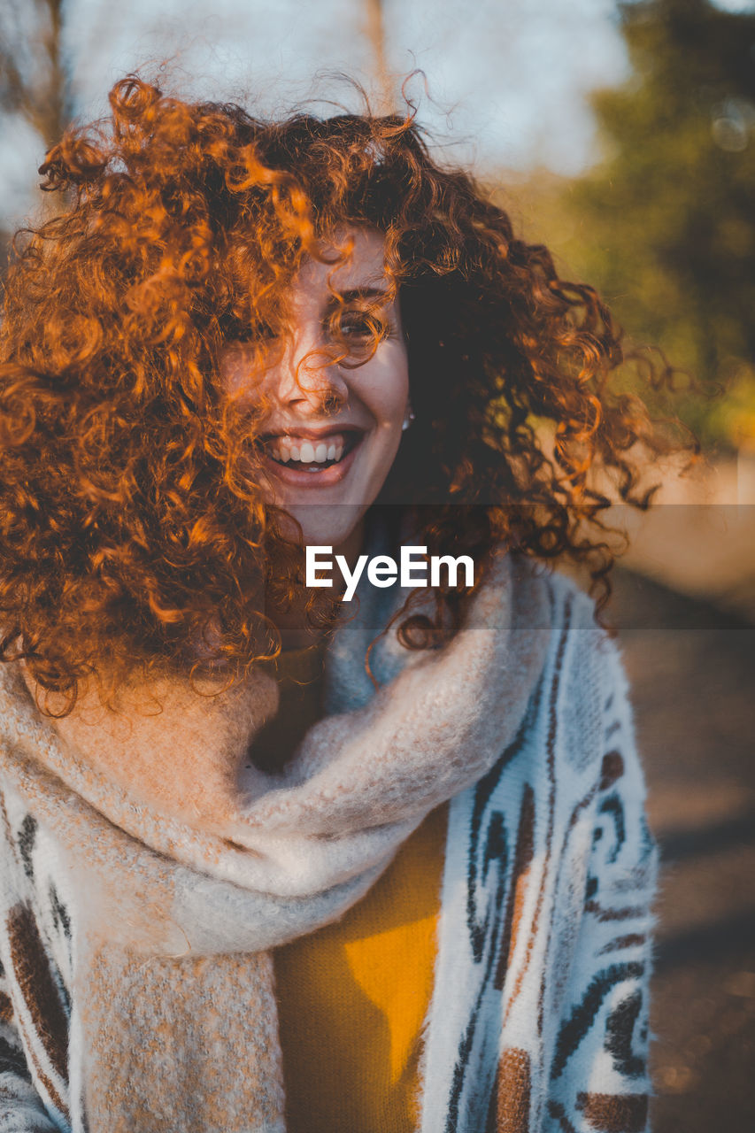 Smiling young woman standing against trees during sunny day