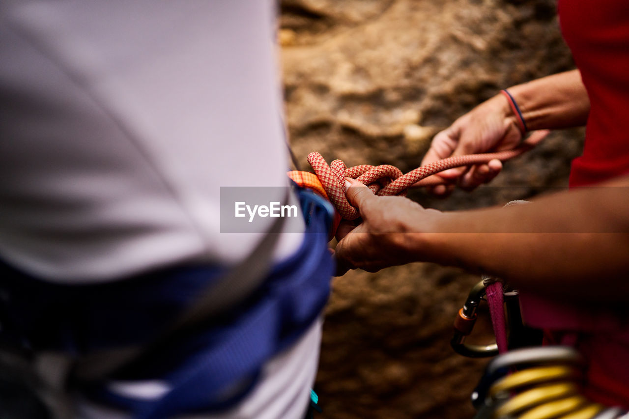 Active cropped unrecognizable woman assisting female friend tying rope on harness while preparing for climbing